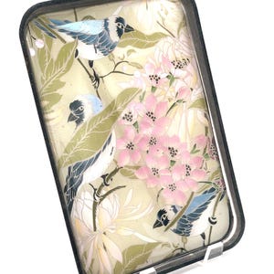 May include: Rectangular decorative tray with a black border. The tray features a design of blue birds, pink flowers, and green leaves on a cream-colored background. The birds have black beaks and are perched on branches.