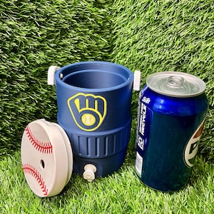 May include: A navy blue beverage cooler with a yellow and white baseball glove logo, featuring a white lid decorated with red baseball stitching, positioned next to a blue aluminum soda can. The cooler has a small white spigot at the base.