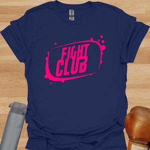 Puede incluir: Una camiseta azul marino con un gráfico rosa de las palabras "Fight Club" en un rectángulo redondeado con salpicaduras rosas.