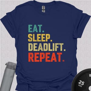 Könnte beinhalten: Ein marineblaues T-Shirt mit einer Grafik im Vintage-Stil, auf dem "Eat. Sleep. Deadlift. Repeat." steht.