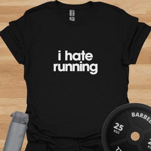 May include: A black short-sleeved t-shirt featuring the white text "i hate running" printed in a bold, sans-serif font across the chest. The garment has a crew neckline and a standard fit, with a visible brand label inside the collar area.