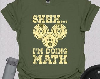 Puede incluir: Una camiseta verde con un gráfico de placas de peso y el texto "SHHH... I'M DOING MATH".