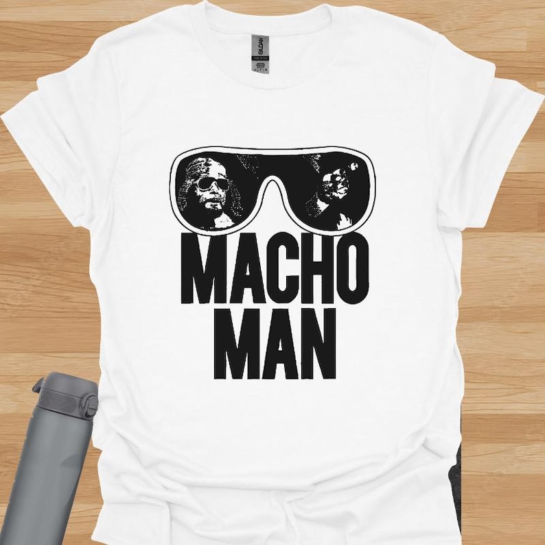 K&ouml;nnte beinhalten: Wei&szlig;es T-Shirt mit einer schwarz-wei&szlig;en Grafik einer Sonnenbrille mit zwei Gesichtern und den Worten "MACHO MAN" in fetten, schwarzen Buchstaben. Das Shirt ist aus einem weichen Material.