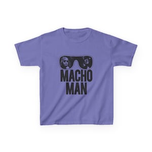 May include: A lilac t-shirt with a black graphic of sunglasses containing two faces, and the words "MACHO MAN" in black below. The shirt is made of a soft material.