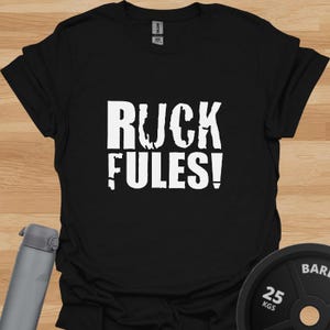 Peut inclure: T-shirt noir avec un texte blanc qui dit "RUCK FULES!"