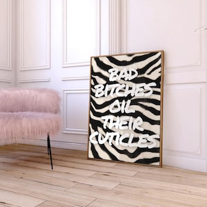 May include: A rectangular framed wall art piece featuring a black and white zebra stripe pattern background with the white text BAD BITCHES OIL THEIR CUTICLES printed in a bold, sans-serif font across the centre of the print.