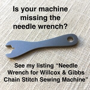 Puede incluir: Una llave de aguja plateada para una m&aacute;quina de coser. La llave tiene un agujero en el mango y una abertura en forma de U en un extremo. El texto "Is your machine missing the needle wrench? See my listing "Needle Wrench for Willcox & Gibbs Chain Stitch Sewing Machine" es visible en la imagen.