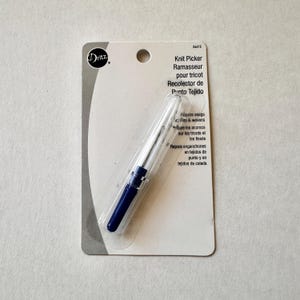 May include: A Dritz Knit Picker tool in its original packaging. The tool has a clear plastic handle with a dark blue grip and a silver metal needle. The packaging includes text in English, French, and Spanish.