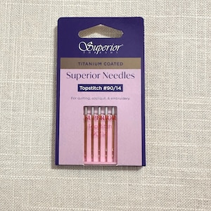 May include: A package of Superior Needles for quilting, appliqué, and embroidery. The package is purple and pink, with the brand name and needle type clearly labeled. The needles are visible through a clear window.