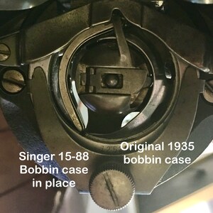 May include: Close-up of a Singer 15-88 bobbin case in place. The case is silver and has a small screw on the side. The text "Original 1935 bobbin case" is visible below the case.