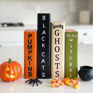 May include: Four rectangular wooden blocks arranged vertically, colored orange, black, cream, and green, with the text PUMPKINS, BLACK CATS, Spooky GHOSTS, and Wicked Witches. Includes a small orange jack-o'-lantern, a black spider, and candy corn.