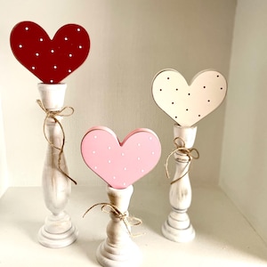 May include: Three decorative heart-shaped candle holders. The hearts are red, pink, and off-white, each with white or black polka dots. The candle holders are white with a distressed finish and tied with twine.