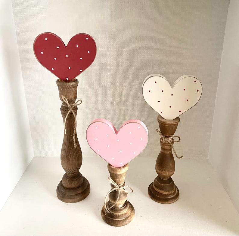 Pode incluir: Tr&ecirc;s decora&ccedil;&otilde;es de madeira em forma de cora&ccedil;&atilde;o. Os cora&ccedil;&otilde;es s&atilde;o vermelhos, rosa e creme, cada um com bolinhas brancas. S&atilde;o montados em casti&ccedil;ais de madeira torneada, amarrados com barbante. Um charmoso item de decora&ccedil;&atilde;o r&uacute;stica.