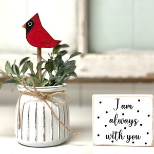 May include: White ceramic planter with a distressed finish and a red cardinal bird figurine. The planter has a twine bow around the top. A small white wooden sign with black text reads "I am always with you".