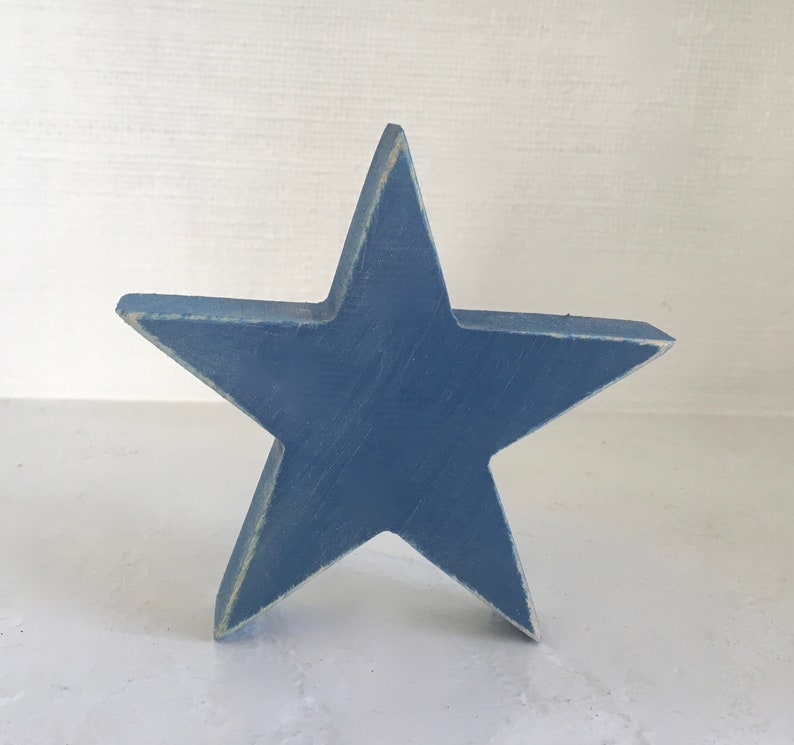 Puede incluir: Una estrella de madera azul con un acabado desgastado. La estrella es un dise&ntilde;o simple de cinco puntas.