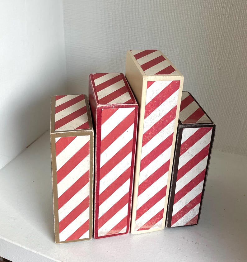 K&ouml;nnte beinhalten: Eine Ansammlung von f&uuml;nf rechteckigen Schachteln mit rot-wei&szlig;en diagonalen Streifen. Die unterschiedlich gro&szlig;en Schachteln sind versetzt angeordnet. Die Schachteln haben eine Vintage-&Auml;sthetik.