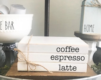 May include: Three white wooden blocks stacked on top of each other with the words "coffee", "espresso", and "latte" written in black on each block. The blocks are tied together with twine.