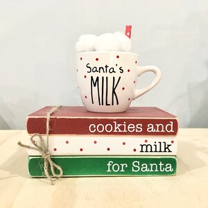 May include: A white ceramic mug with red polka dots and the text "Santa's MILK" sits on top of three stacked wooden blocks. The blocks are painted red, white with red polka dots, and green. The top block has the text "cookies and", the middle block has the text ".milk", and the bottom block has the text "for Santa".