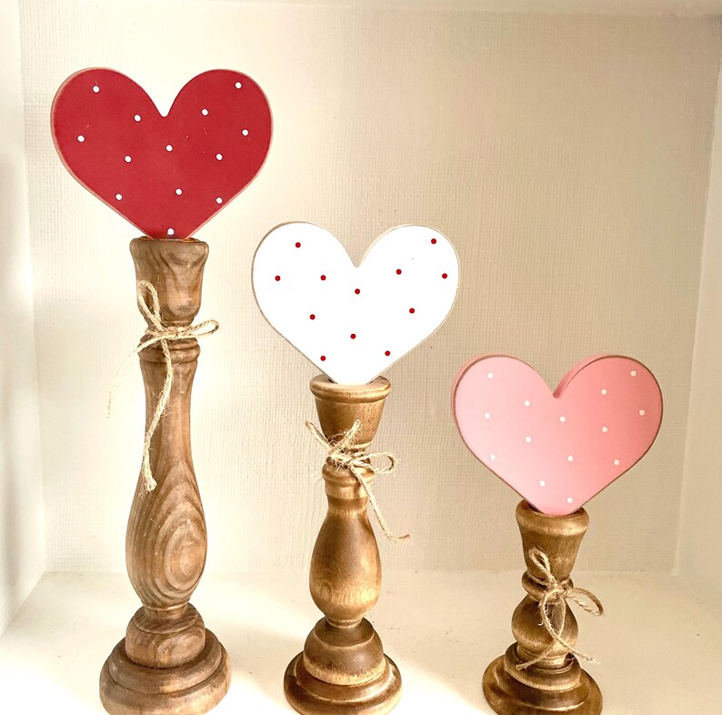 Pode incluir: Tr&ecirc;s decora&ccedil;&otilde;es de cora&ccedil;&atilde;o de madeira. Os cora&ccedil;&otilde;es s&atilde;o vermelhos, brancos e rosa, cada um com bolinhas brancas. S&atilde;o montados em casti&ccedil;ais de madeira e amarrados com barbante. O mais alto tem aproximadamente 30 cm de altura.