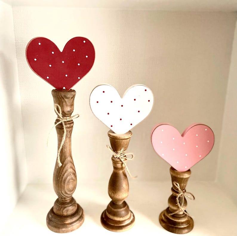 Pode incluir: Tr&ecirc;s decora&ccedil;&otilde;es de madeira em forma de cora&ccedil;&atilde;o. Cada cora&ccedil;&atilde;o &eacute; montado em um casti&ccedil;al de madeira. Os cora&ccedil;&otilde;es s&atilde;o vermelhos, brancos e rosa, cada um com bolinhas brancas. Os casti&ccedil;ais marrons s&atilde;o amarrados com barbante.