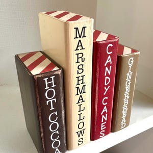 K&ouml;nnte beinhalten: Set aus vier Holz-Buchst&uuml;tzen mit festlichem Thema. Jede Buchst&uuml;tze ist in einer anderen Farbe bemalt: Braun, Creme, Rot und Beige. Die W&ouml;rter "Hot Cocoa", "Marshmallows", "Candy Canes" und "Gingerbread" sind vertikal aufgedruckt.