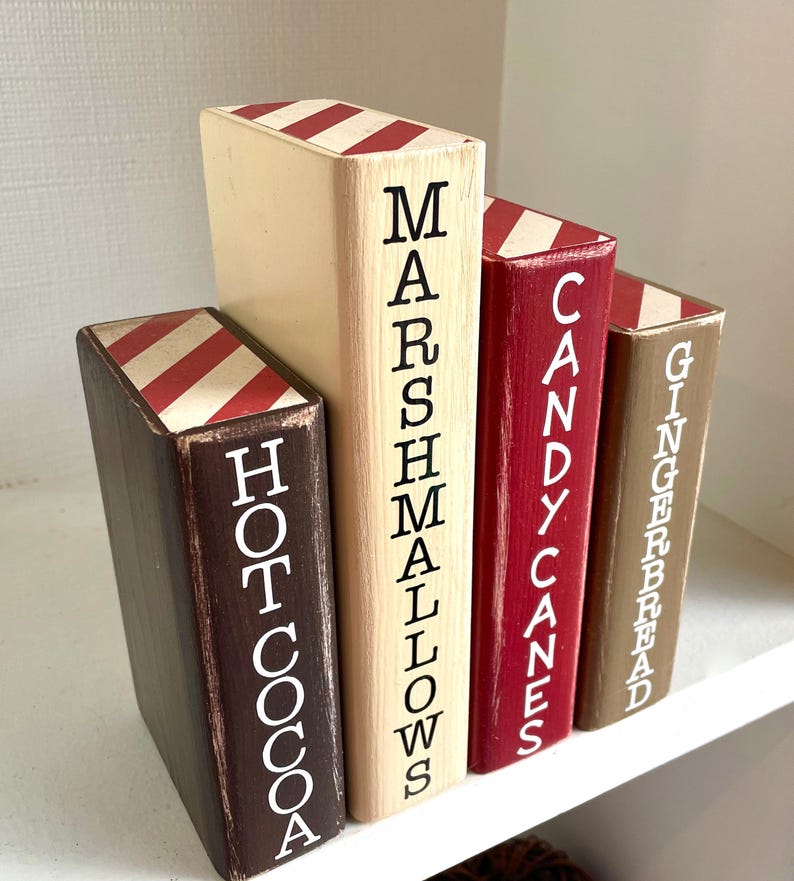 K&ouml;nnte beinhalten: Set aus vier Holz-Buchst&uuml;tzen mit festlichem Thema. Jede Buchst&uuml;tze ist in einer anderen Farbe bemalt: Braun, Creme, Rot und Beige. Die W&ouml;rter "Hot Cocoa", "Marshmallows", "Candy Canes" und "Gingerbread" sind vertikal aufgedruckt.