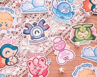 May include: A collection of colorful stickers featuring cartoon characters and motivational phrases. The stickers include images of cute creatures with phrases like "stay hydrated," "positive energy," and "fear me." The stickers are on a lace surface.