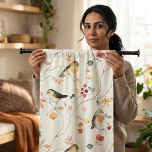 May include: Cream-colored curtain panel featuring a watercolor design of birds perched on branches with leaves, berries, and flowers in shades of orange, red, and green. The curtain is held up by a black rod.