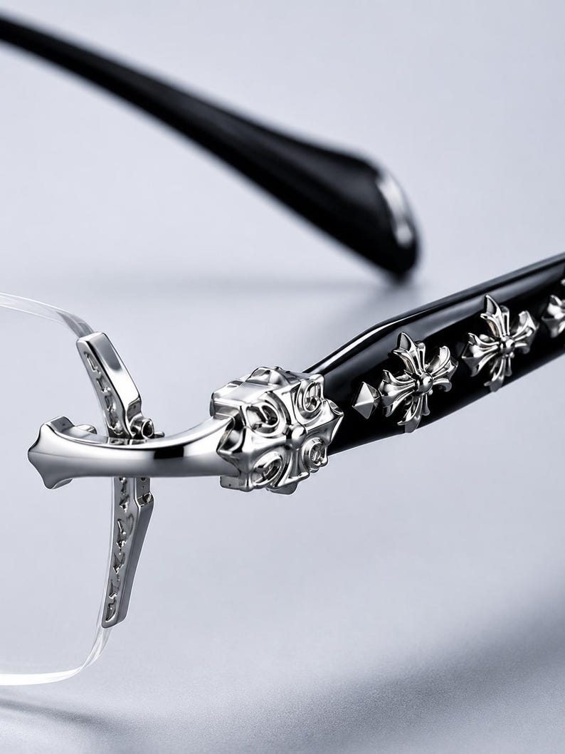 K&ouml;nnte beinhalten: Randlose Brille mit schwarzen B&uuml;geln, die mit silberfarbenen Kreuzemblemen aus Metall verziert sind. Der Scharnierbereich zeigt ein detailliertes silberfarbenes Kreuzdesign, das mit der Glasfassung verbunden ist und ein dekoratives Element bildet.