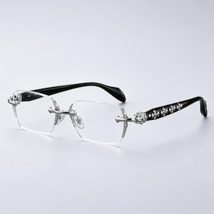 May include: Rimless eyeglasses featuring clear rectangular lenses and silver-tone metal hardware at the bridge and hinges. The temples are black with a series of decorative silver-tone cross emblems embedded along the outer sides of the arms.