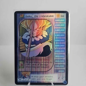 Puede incluir: Carta coleccionable con Goku, el Imbatible, con un diseño holográfico. La carta muestra una ilustración de Goku e incluye texto con niveles de poder e instrucciones del juego. La carta está protegida en una funda transparente.