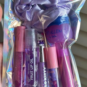Peut inclure: Une pochette holographique contenant un chouchou en satin violet clair, un brillant à lèvres rose pailleté, une huile à lèvres au raisin, un brillant à lèvres Hello Kitty, un petit brillant à lèvres rose et un baume à lèvres Tim Allen violet.