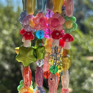 May include: A collection of four beaded keychains featuring colorful plastic charms. The strands include various shapes such as flowers, mushrooms, stars, and fish in shades of pink, yellow, green, blue, and red, all attached to silver metal clasps.