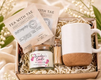 May include: A gift box containing two Tea With Tae sachets, a white ceramic mug with a cork base, a small glass jar of matches with a cork stopper, and a glass jar candle labeled Grandma's Candle White Sage & Lavender Scented 100% Soy Candle.