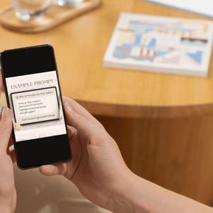 Puede incluir: Un tel&eacute;fono inteligente muestra el texto "EXAMPLE PROMPT" en la parte superior. La pantalla muestra una indicaci&oacute;n para los vendedores de Etsy, incluida la redacci&oacute;n de una descripci&oacute;n del producto, la resaltaci&oacute;n de palabras clave y la generaci&oacute;n de ahorros. El tel&eacute;fono se sostiene frente a un fondo borroso.