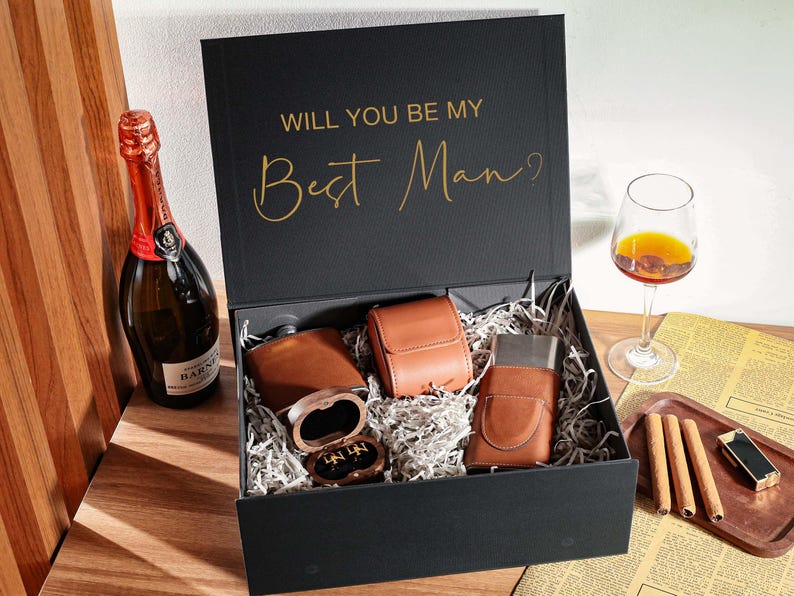 Peut inclure: Une bo&icirc;te cadeau noire avec le texte dor&eacute; WILL YOU BE MY Best Man? contenant une flasque gain&eacute;e de cuir marron, un petit &eacute;tui en cuir marron, un briquet gain&eacute; de cuir marron et une petite bo&icirc;te en bois avec des boutons de manchette.