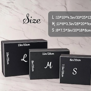 Peut inclure: Trois bo&icirc;tes cadeaux rectangulaires noires en tailles grande, moyenne et petite. Chaque bo&icirc;te porte une lettre blanche L, M ou S. Les dimensions sont indiqu&eacute;es : L mesure 33x25x12 cm, M mesure 28x20x9 cm et S mesure 20x18x8 cm.