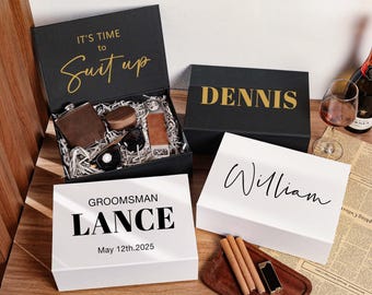 May include: Three gift boxes with personalized names, "Dennis", "William", and "Groomsman Lance", with the date "May 12th, 2025". The box labeled "Groomsman Lance" is open and contains a brown flask, a small wooden box, a pair of sunglasses, and a brown leather strap.
