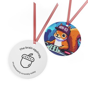 May include: Two white, round ornaments with red ribbons. One features an acorn graphic and the text "The brain squirrels are particularly scrambly today." The other shows a pixelated squirrel wearing a hat that says "ADH-DJ" and is behind a DJ mixing board.
