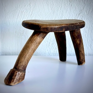 May include: A rustic wooden stool with three legs. The stool is made of natural wood and has a simple, organic design.