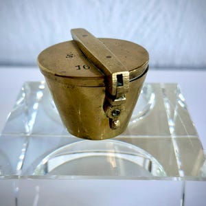 May include: A small, brass, hinged container with a lid. The container is marked with the number "16" and the letter "S".