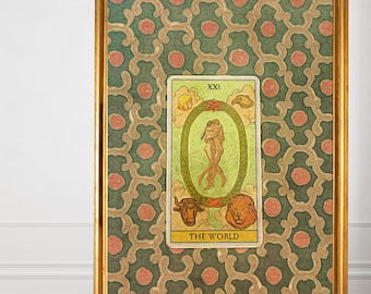 Peut inclure: Impression encadrée de la carte de tarot "Le Monde". La carte est placée sur un fond à motifs verts et dorés et encadrée dans un cadre doré. L'impression est exposée sur un sol en bois.