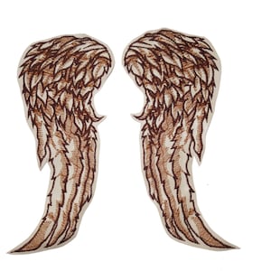 Puede incluir: Dos parches bordados con forma de alas de ángel. Las alas son marrones con detalles en beige y crema. Los parches son probablemente para ropa o proyectos de manualidades.