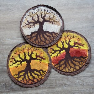 Pode incluir: Três patches redondos bordados com um desenho de árvore. Os patches têm uma borda marrom e retratam árvores com raízes e galhos detalhados. A paleta de cores inclui tons de marrom, amarelo e laranja, criando uma estética quente e terrosa.