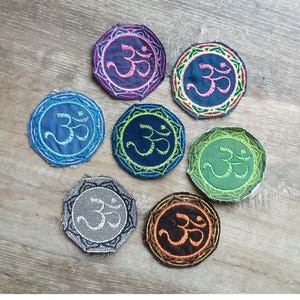 May include: Seven embroidered patches with the Om symbol in various colors, including purple, blue, green, and orange. Each patch has a circular design with a decorative border. The patches are arranged on a wooden surface.