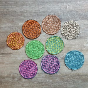 Puede incluir: Un conjunto de parches circulares con un diseño geométrico de la flor de la vida. Los parches son de varios colores, como naranja, marrón, verde, rosa y azul. Los parches están hechos de tela y tienen un borde cosido.