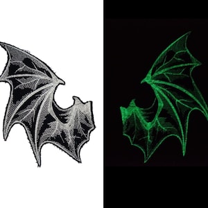 May include: Embroidered bat wing patch. One wing is black with silver stitching, the other glows green against a black background. The patch has a detailed, textured design, perfect for jackets or bags.