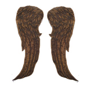 Puede incluir: Dos alas de ángel de tela marrón con patrones de plumas detallados. Las alas son simétricas y parecen estar hechas de un material texturizado, posiblemente para un disfraz o proyecto de manualidades. Fondo blanco.