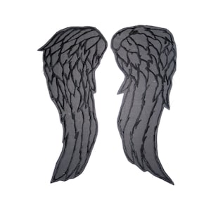 Può includere: Un paio di ali d'angelo nere con un design ricamato dettagliato. Le ali sono realizzate in un tessuto spesso e testurizzato.