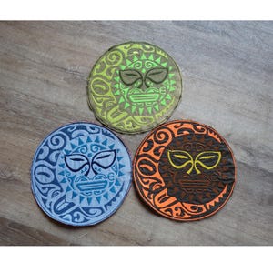 Könnte beinhalten: Drei runde, gestickte Aufnäher mit einem Sonnen-Gesicht-Design. Einer ist blau, einer grün und einer orange. Jeder Aufnäher hat ein detailliertes Stammesmuster und ein Gesicht mit stilisierten Augen und Mund.